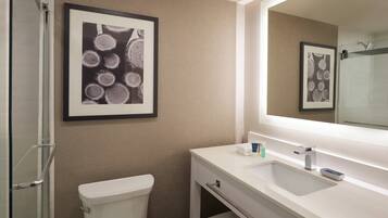A modern bathroom with a toilet, sink, and shower. There is a framed picture on the wall and a mirror above the sink.