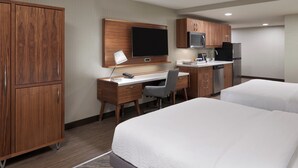 Una habitación de hotel con un escritorio de madera, televisión, microondas, refrigerador y dos camas.