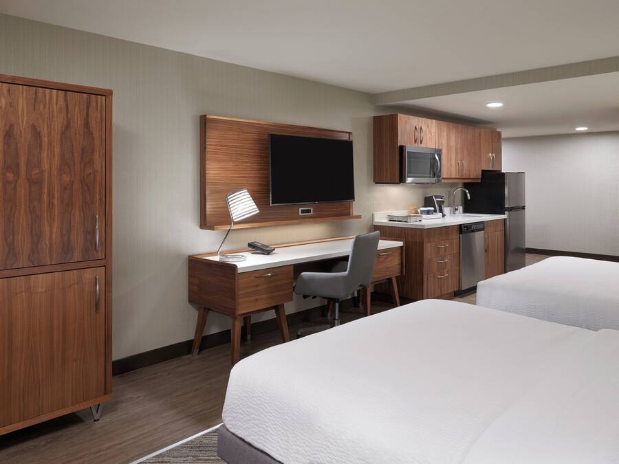 A hotel room with a wooden desk, a television, a microwave, a refrigerator, and two beds.
