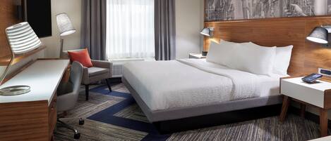 A hotel room with a large bed, a desk, a chair, a TV, and a painting on the wall.