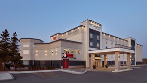 Un hotel moderno con restaurante Boston Pizza, zona de estacionamiento techada y una entrada bien iluminada.