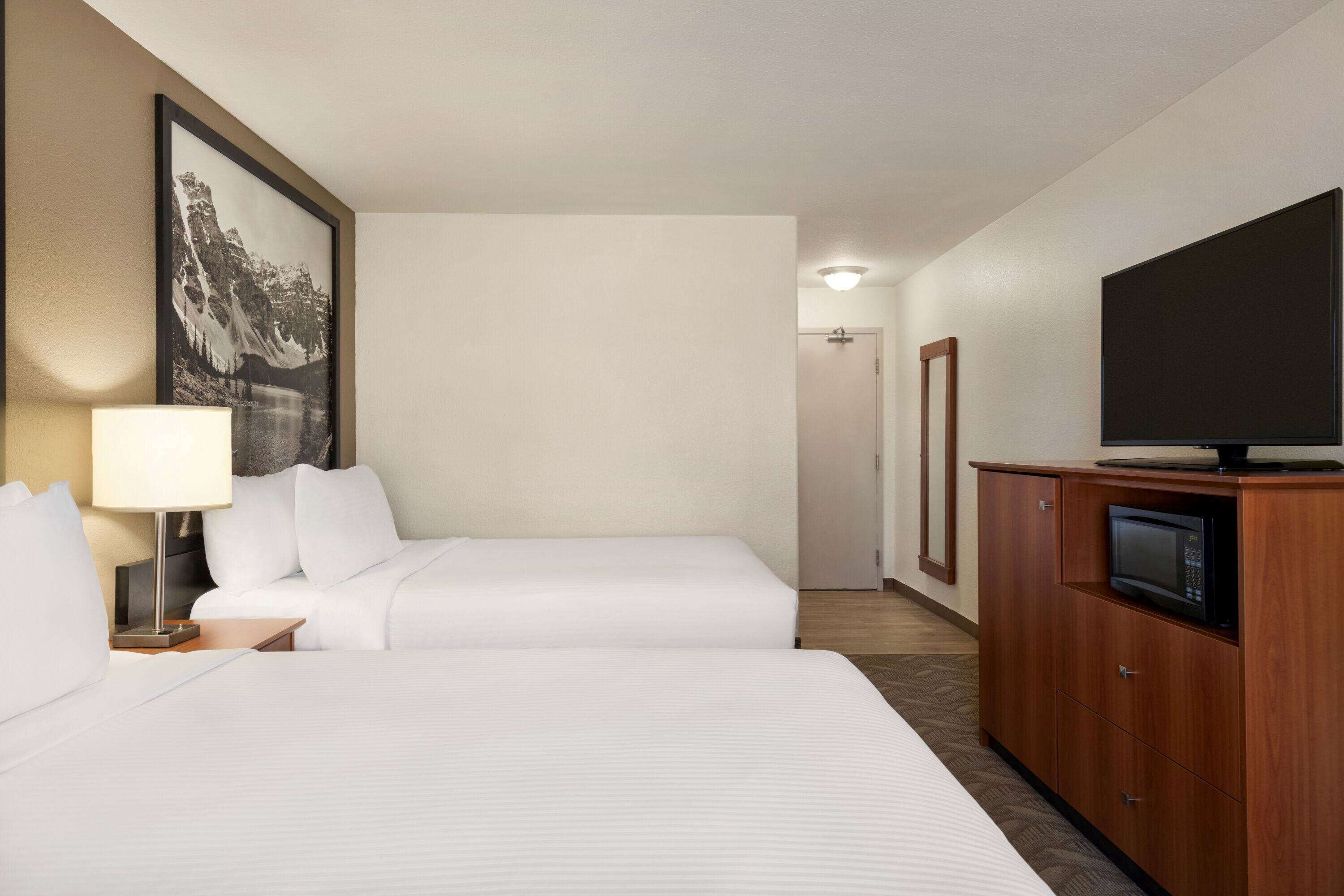 A hotel room with two beds, a television on a wooden cabinet, and a framed picture on the wall.