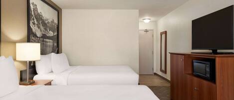 A hotel room with two beds, a television on a wooden cabinet, and a framed picture on the wall.