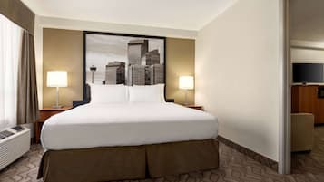 Habitación de hotel con una cama grande, dos lámparas de noche, un cuadro con una vista urbana y un televisor sobre un soporte de madera.