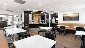 A modern restaurant with white tables and black chairs, a counter with a coffee machine, and a large painting on the wall. - Super 8 by Wyndham Calgary Shawnessy Area (Calgary)