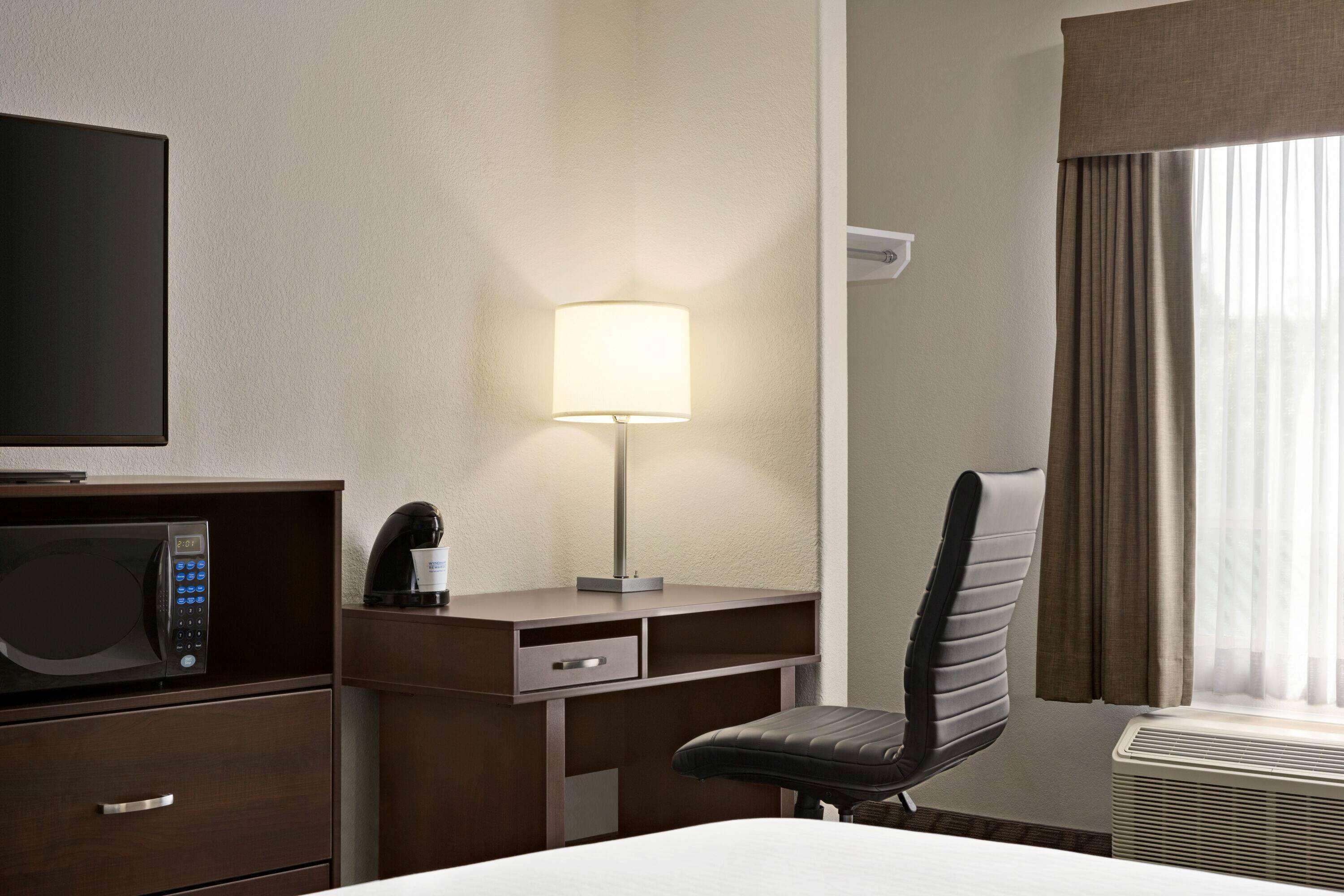 Habitación de hotel con cama, escritorio con lámpara, silla, microondas y televisor.