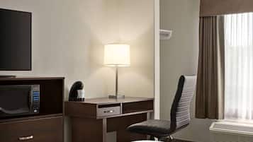 Habitación de hotel con cama, escritorio con lámpara, silla, microondas y televisor.