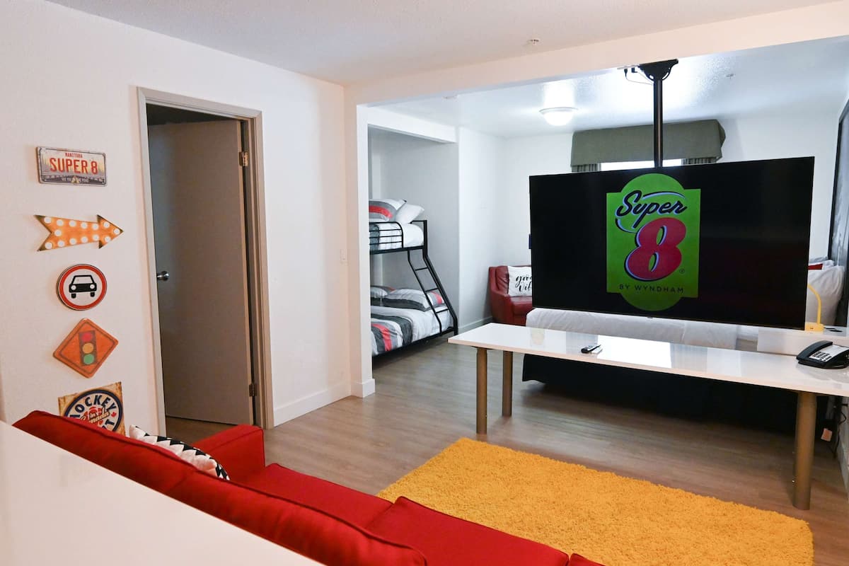 A living room with a red sofa, a white coffee table, and a TV displaying 'Super 8'.