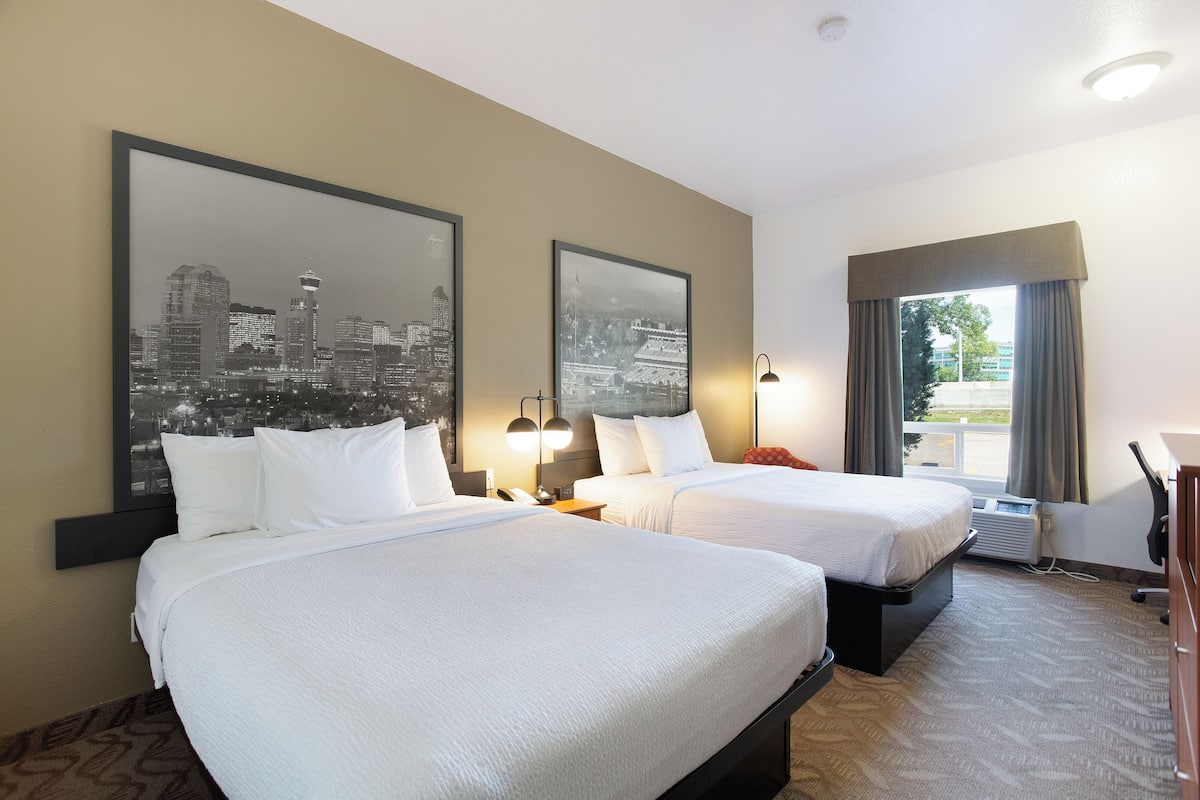 Habitación de hotel con dos camas, vistas a la ciudad, un escritorio y una ventana con cortinas.