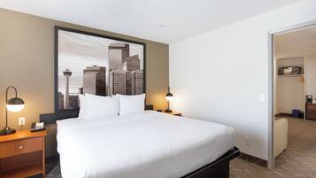 A hotel room with a large bed, two bedside lamps, a cityscape view, a small desk, and a closet.