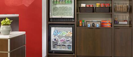 A kitchenette with a refrigerator stocked with beverages, a freezer with ice cream, and shelves with snacks and condiments.