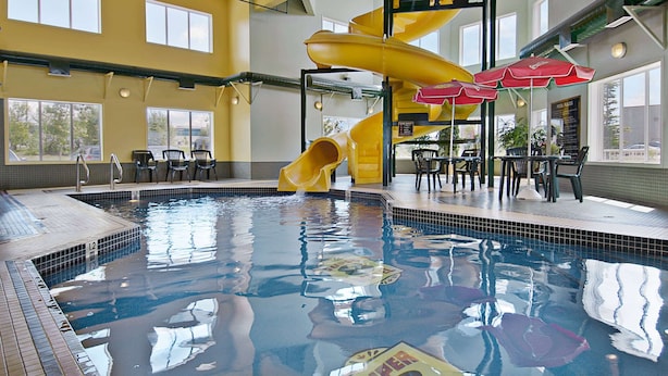 A swimming pool with a yellow slide and red umbrellas, surrounded by chairs and tables. - Super 8 by Wyndham Calgary Shawnessy Area (Calgary)