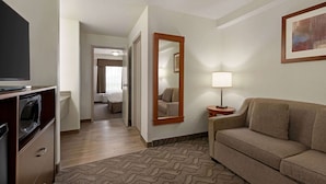 A hotel room with a sofa, a TV, a lamp, a mirror, and a door leading to a bathroom. - Super 8 by Wyndham Calgary Shawnessy Area (Calgary)