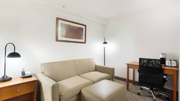A hotel room with a beige sofa, a desk with a lamp, a computer, and a framed picture on the wall.