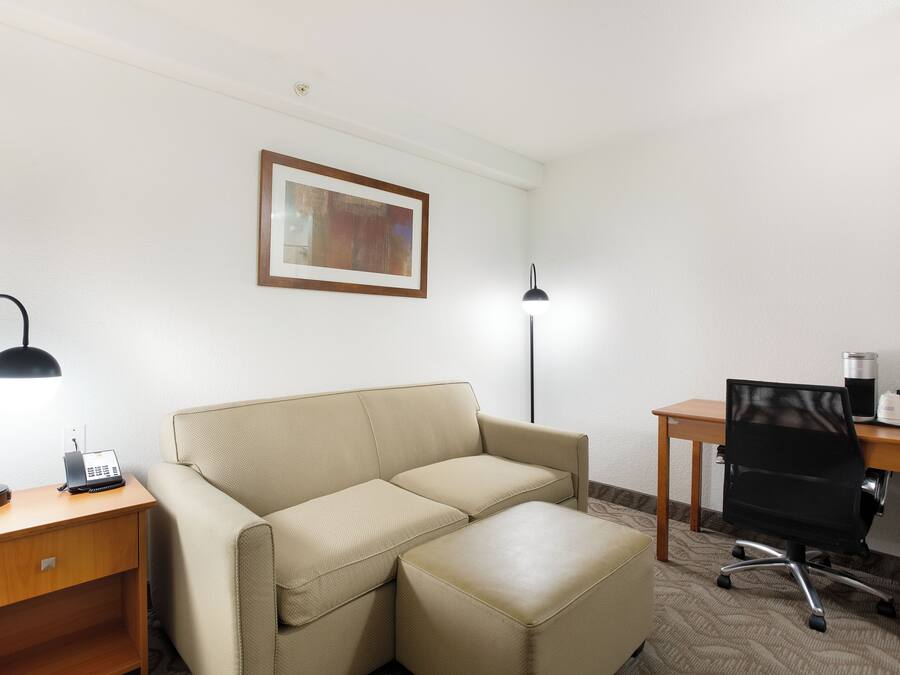 A hotel room with a beige sofa, a desk with a lamp, a computer, and a framed picture on the wall.