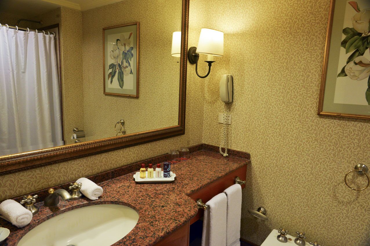 A bathroom with a marble sink, a large mirror, a telephone, and a framed floral painting on the wall.