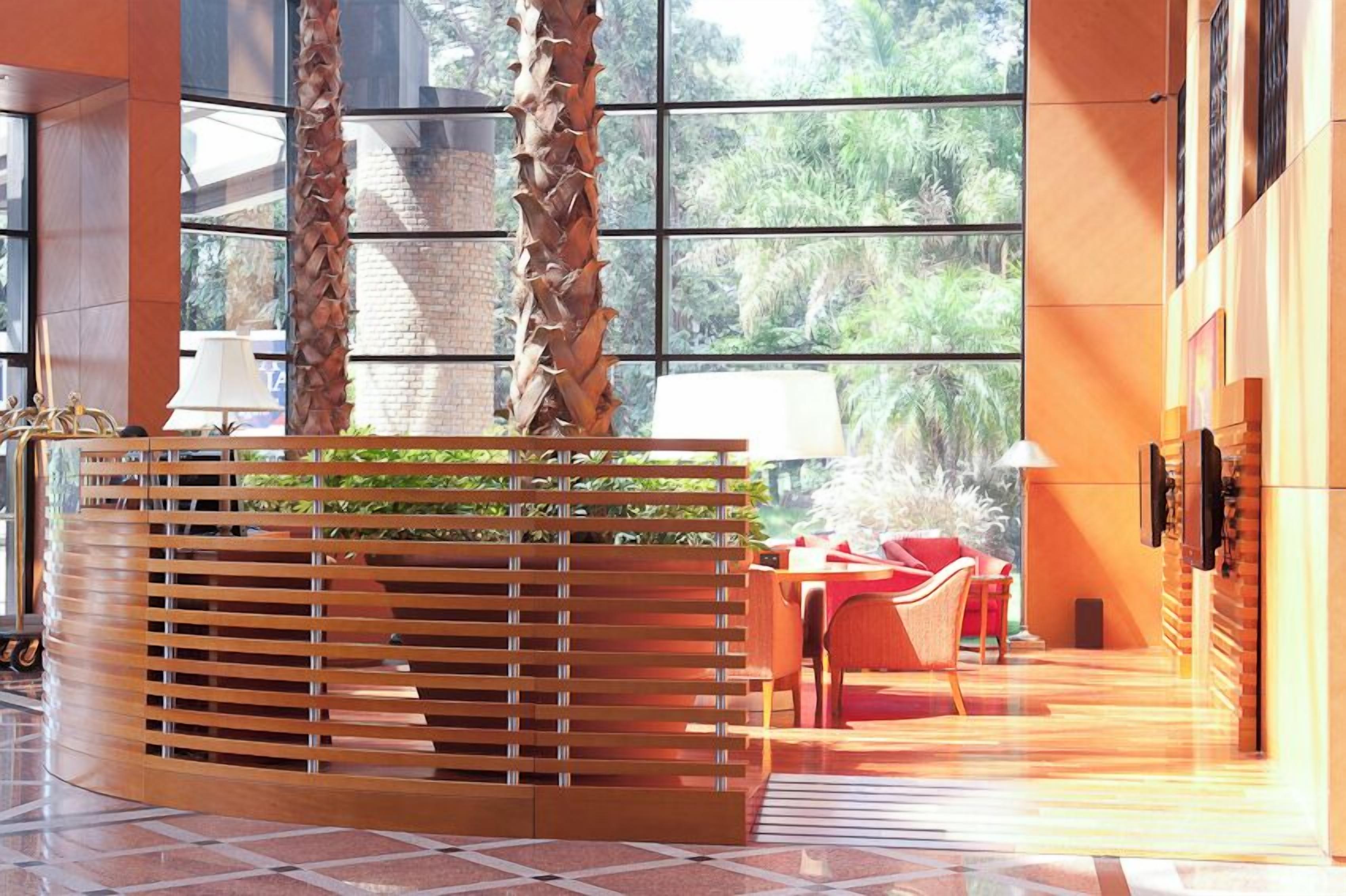 En moderne lobby med en træreception, en rød sofa og et stort vindue med udsigt til grønne områder.