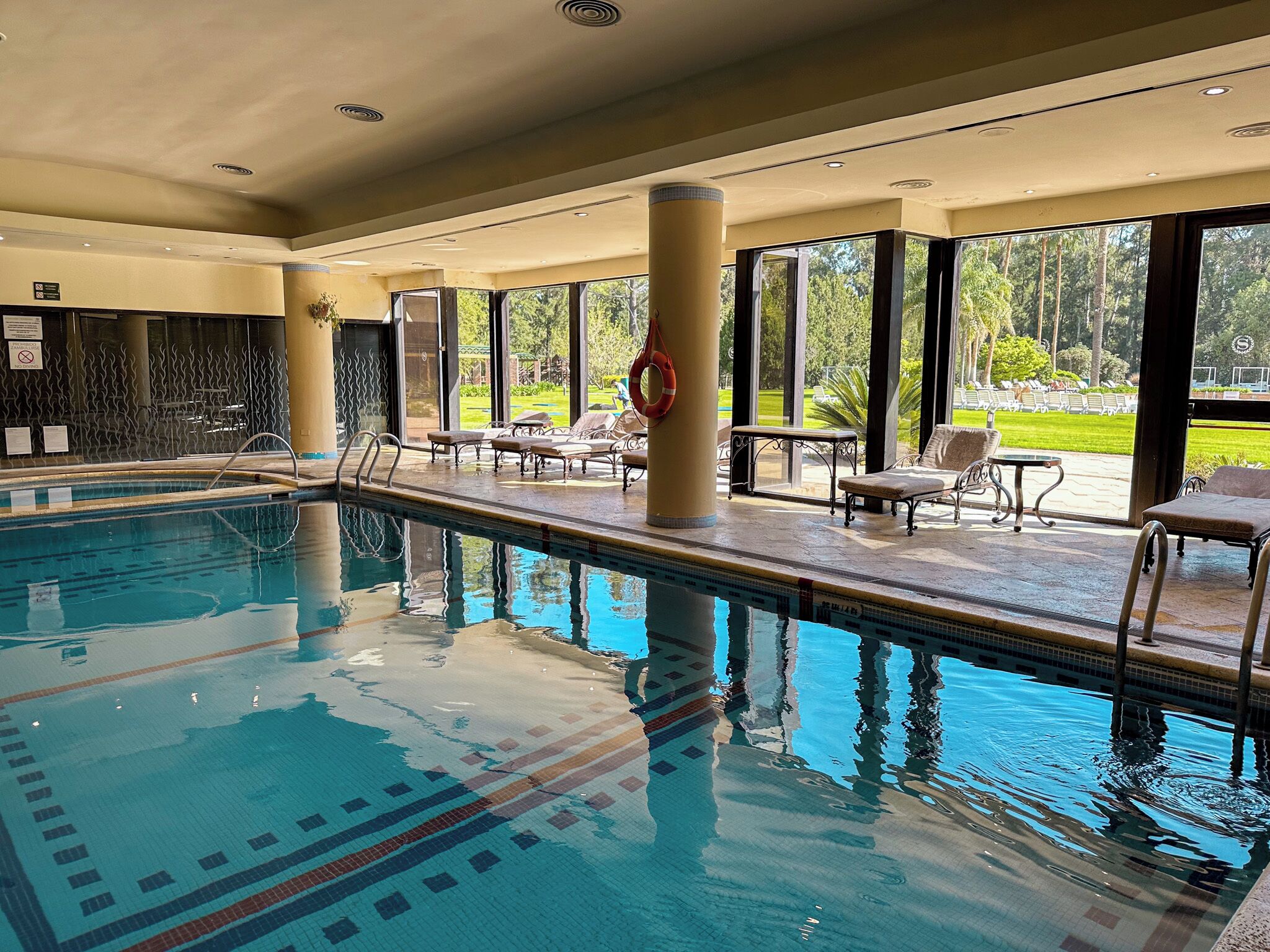 Una piscina con agua cristalina, rodeada de sillones de descanso y vistas a un jardín.