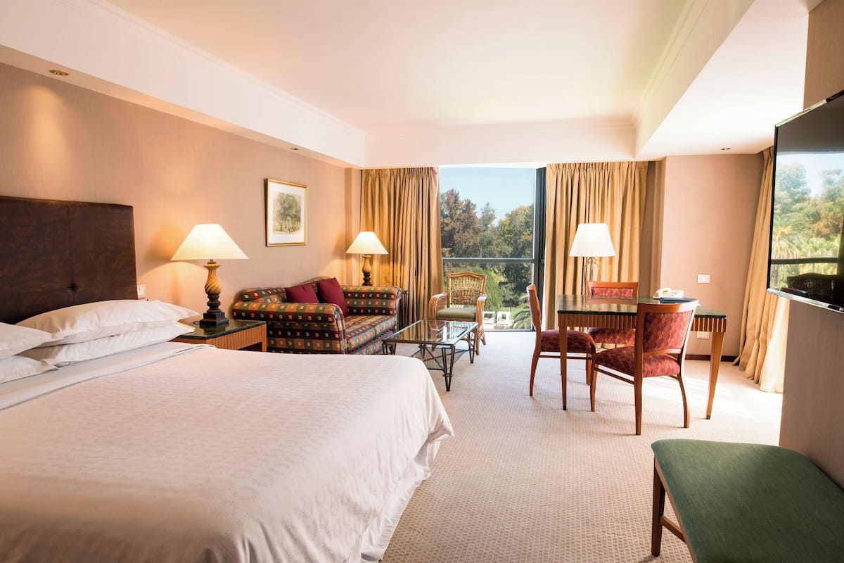 Ein Hotelzimmer mit einem großen Bett, einer Couch, einem Esstisch mit Stühlen und einem Balkon mit Vorhängen.