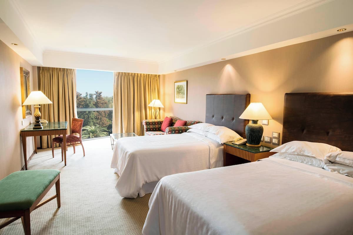 Ein Hotelzimmer mit zwei Betten, einem Schreibtisch, einem Stuhl und Blick ins Freie.