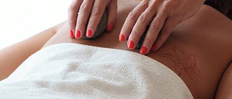A person receiving a massage with a stone on their back.