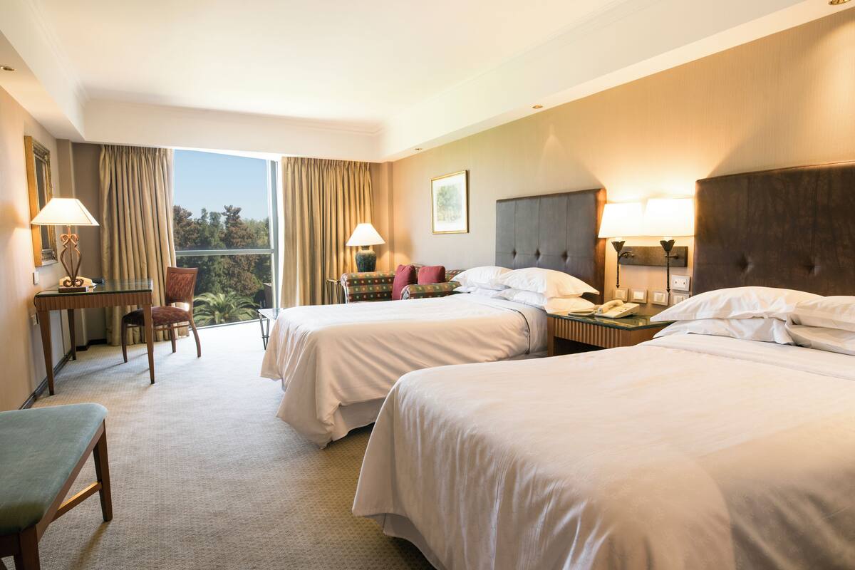 Ein Hotelzimmer mit zwei Betten, einem Schreibtisch, einem Stuhl und Blick ins Freie.
