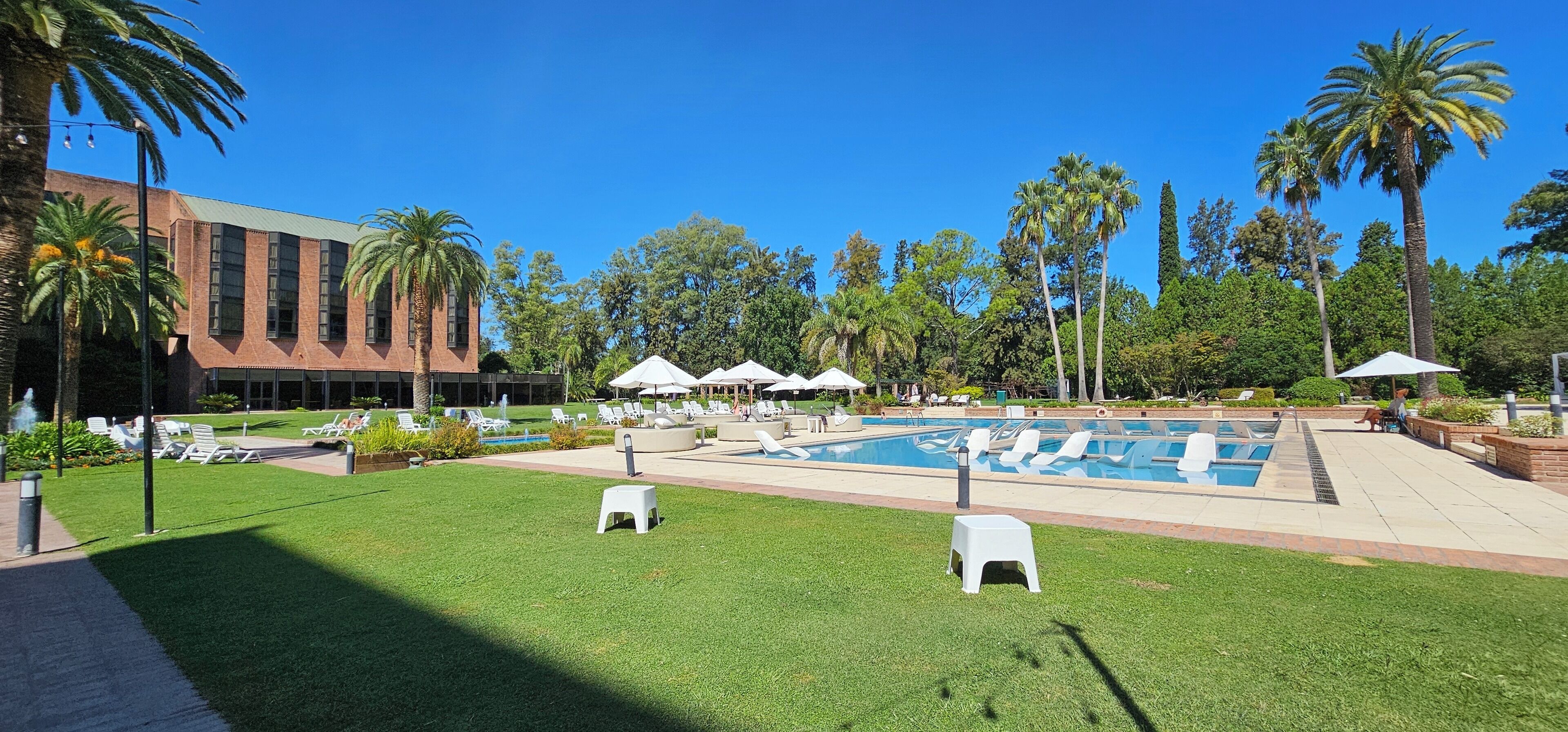 A pool area with lounge chairs, umbrellas, and a building in the background.