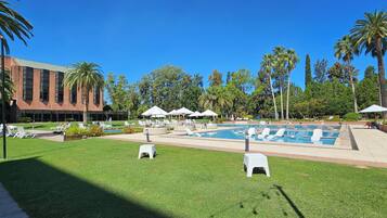 A pool area with lounge chairs, umbrellas, and a building in the background.