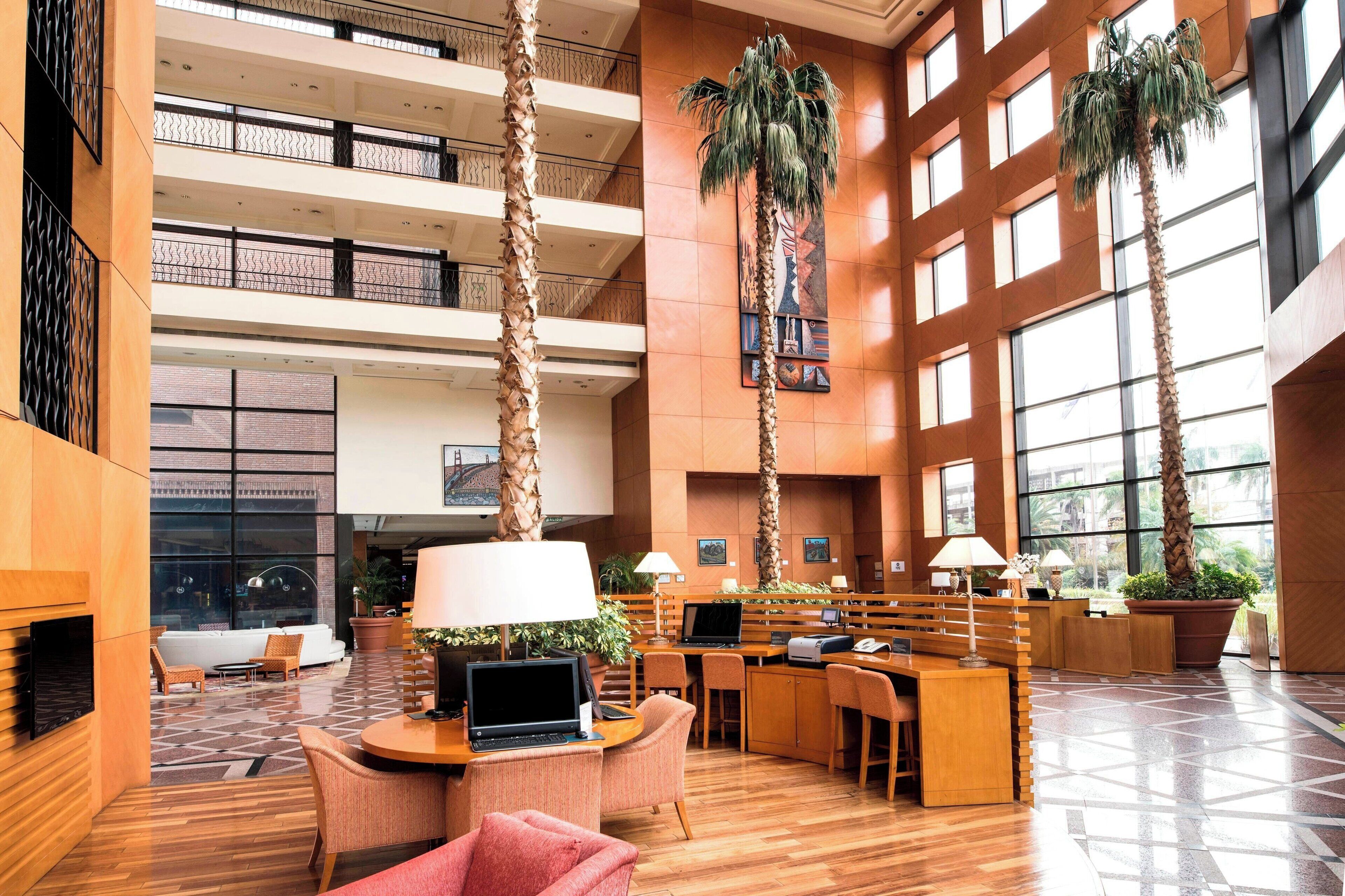 A spacious lobby with multiple seating areas, a reception desk, and tall palm trees.