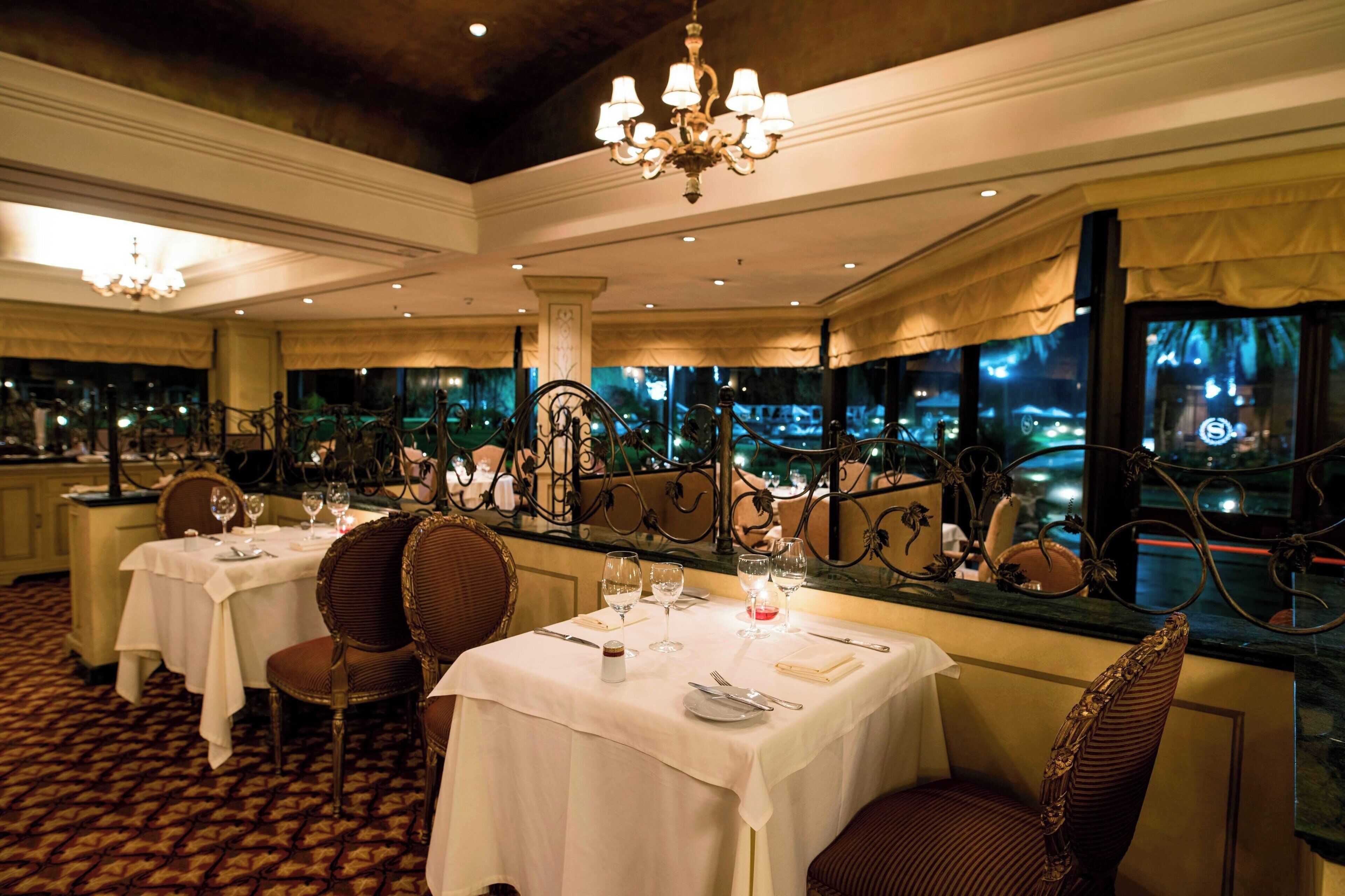 A restaurant with tables set for dining, chairs, and a chandelier.
