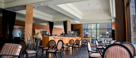 A spacious indoor seating area with multiple chairs and tables, a bar counter, and large windows allowing natural light.