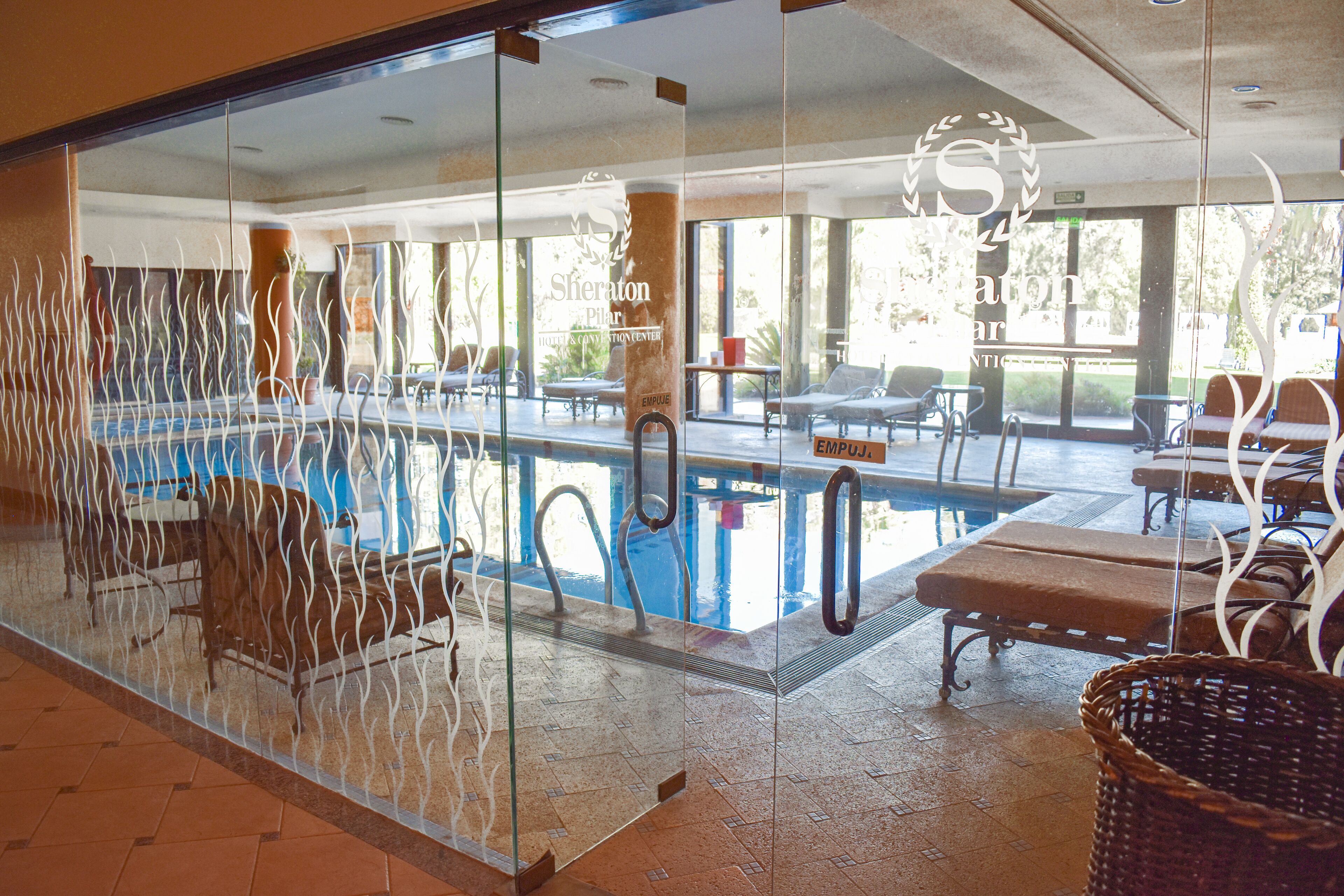 A pool area with lounge chairs and a glass partition.