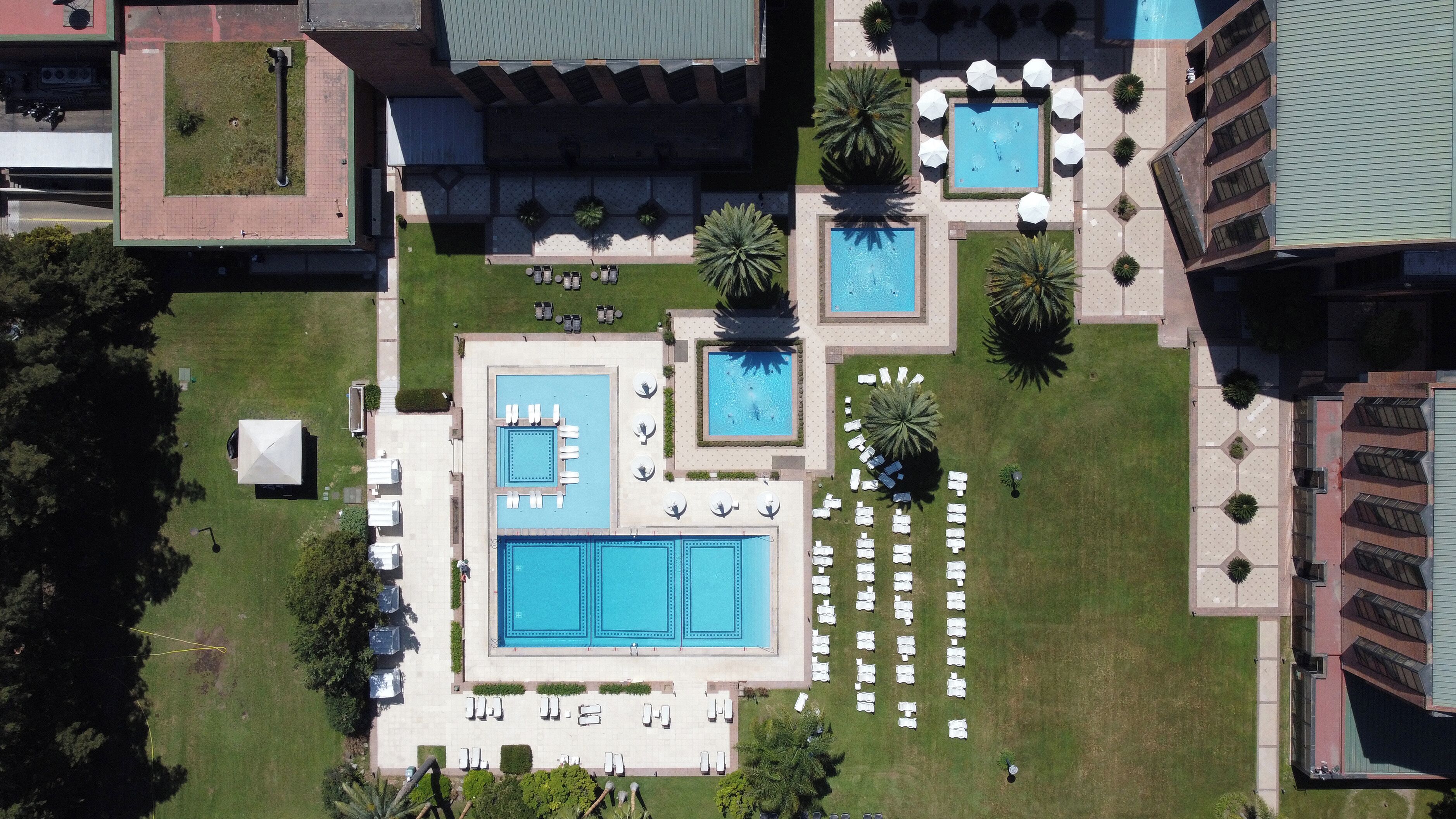 Vista aérea de un hotel con múltiples piscinas, tumbonas y un césped bien cuidado.