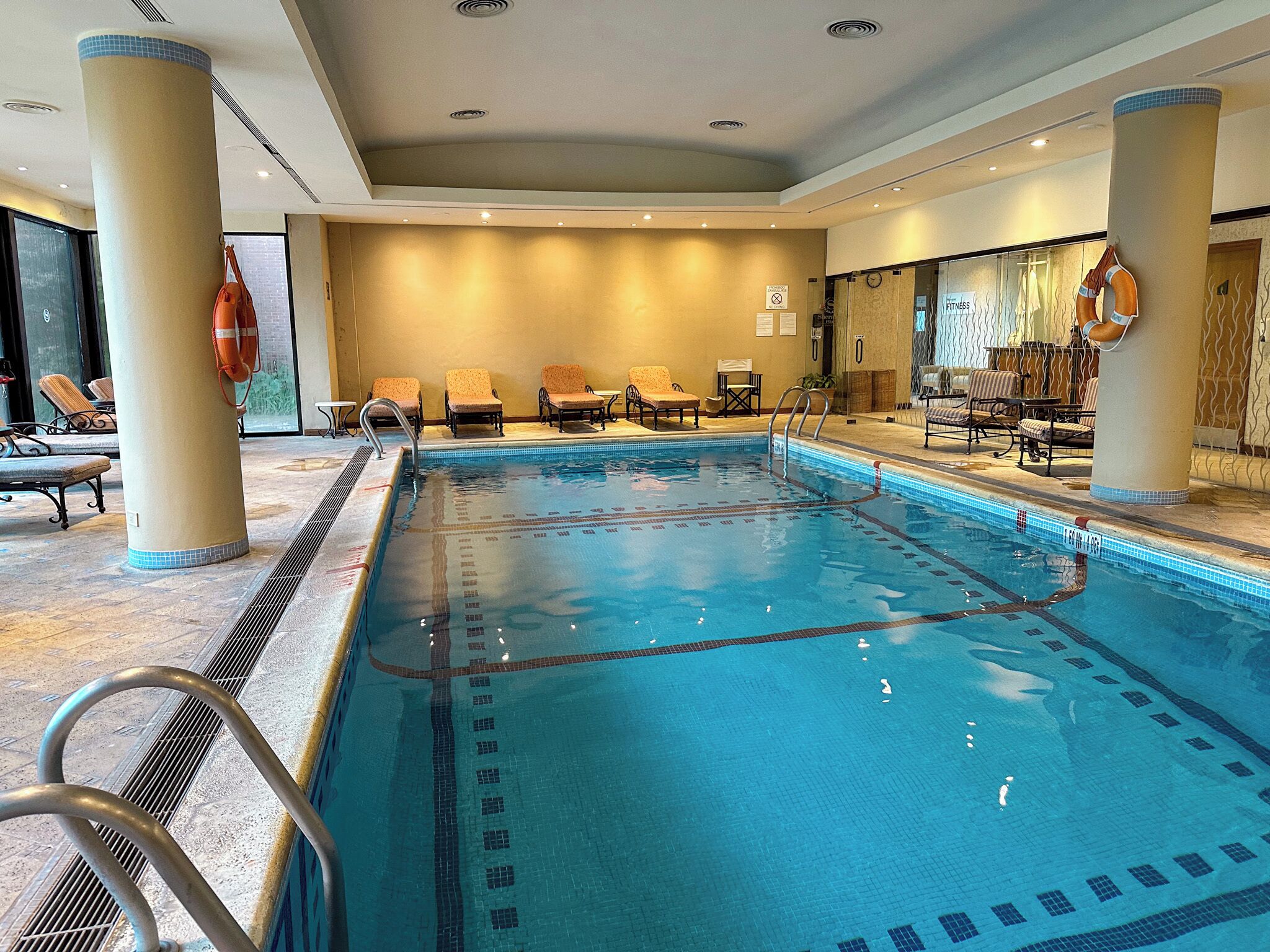 An indoor swimming pool with clear lane markings, lounge chairs, and a lifebuoy on a column.