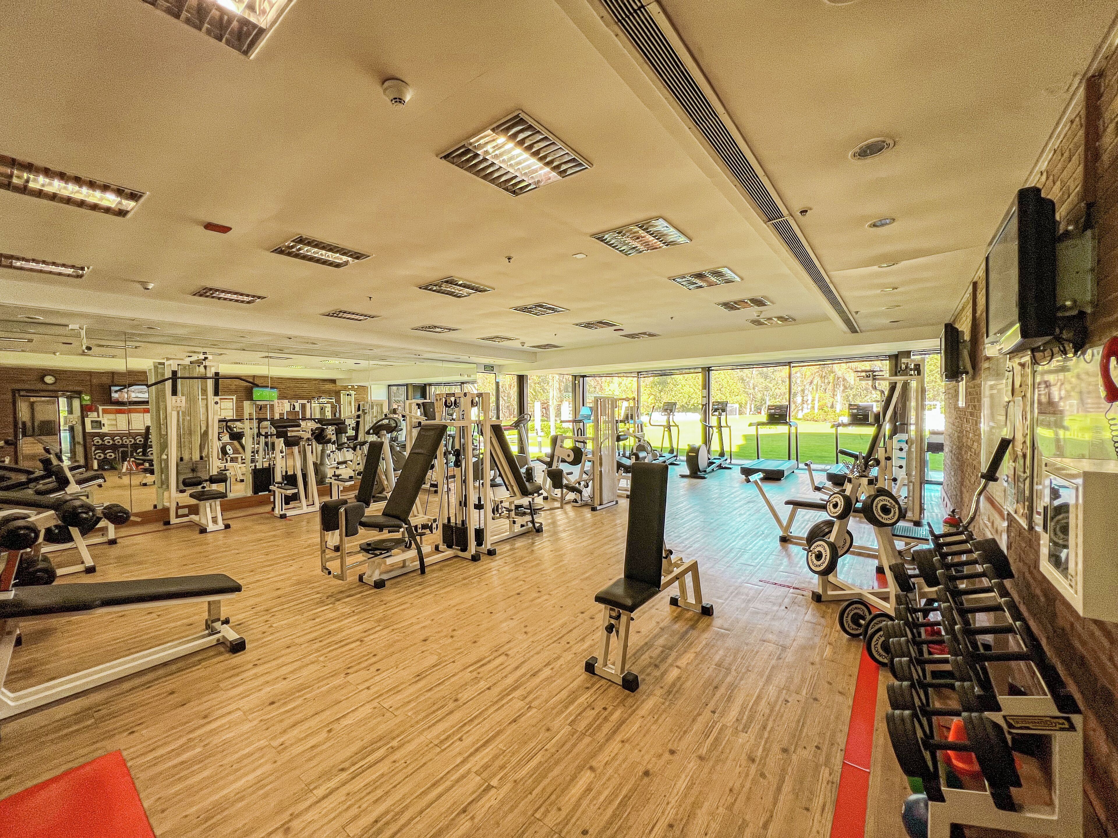 A gym with various exercise equipment, large windows, and a wooden floor.