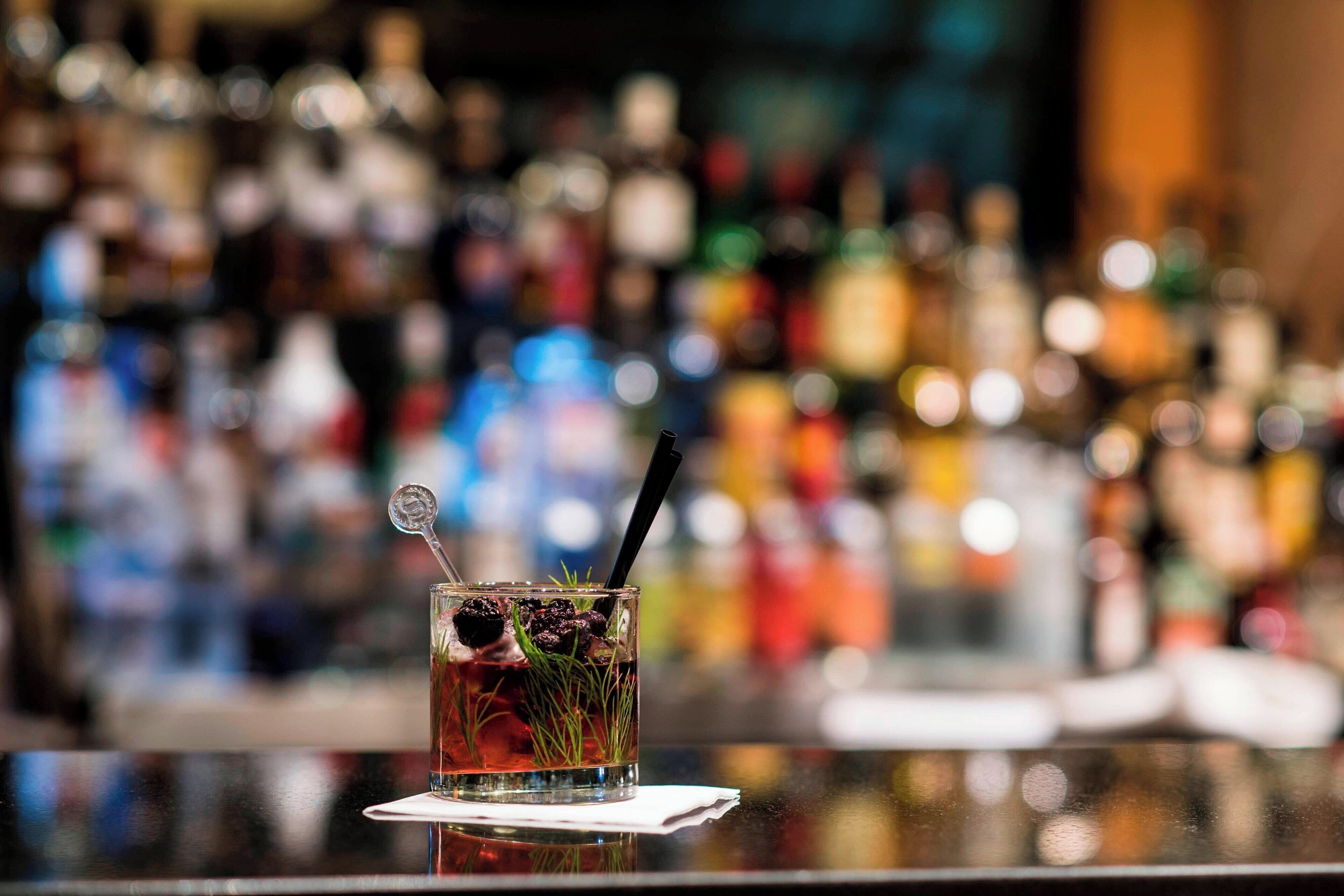 A bar setting with a glass of drink on a coaster, a spoon, and a straw.