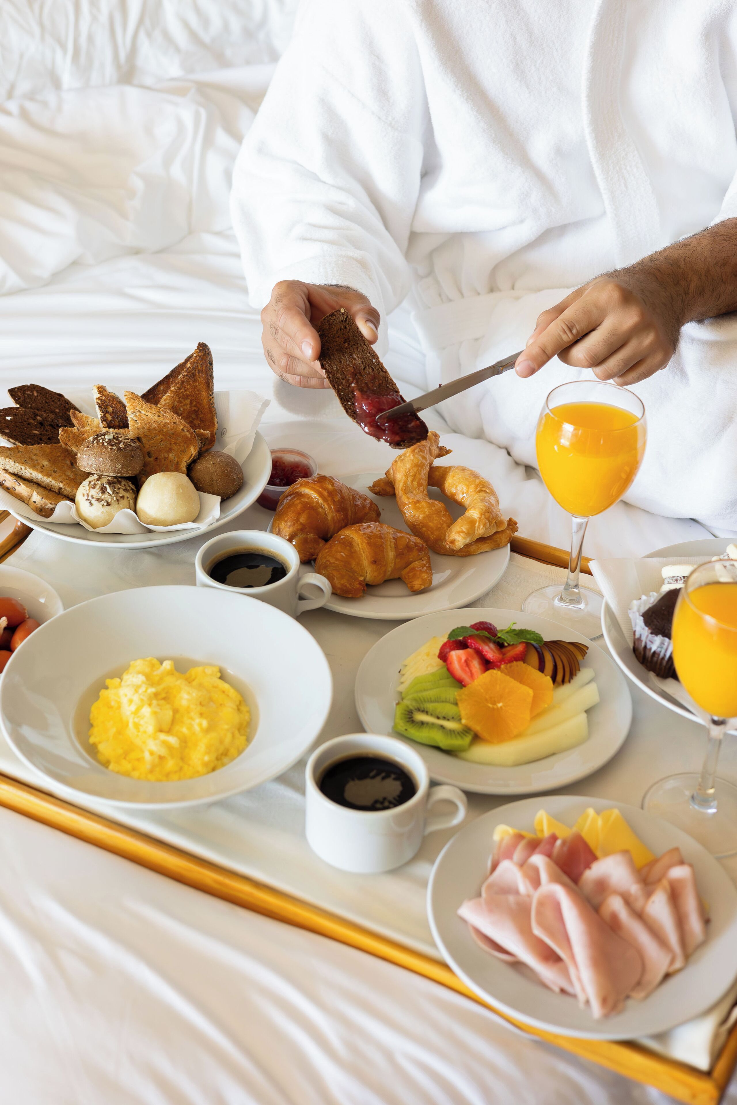 A breakfast tray with croissants, eggs, ham, and fruit on a bed.