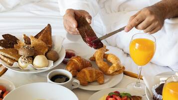 A breakfast tray with croissants, eggs, ham, and fruit on a bed.