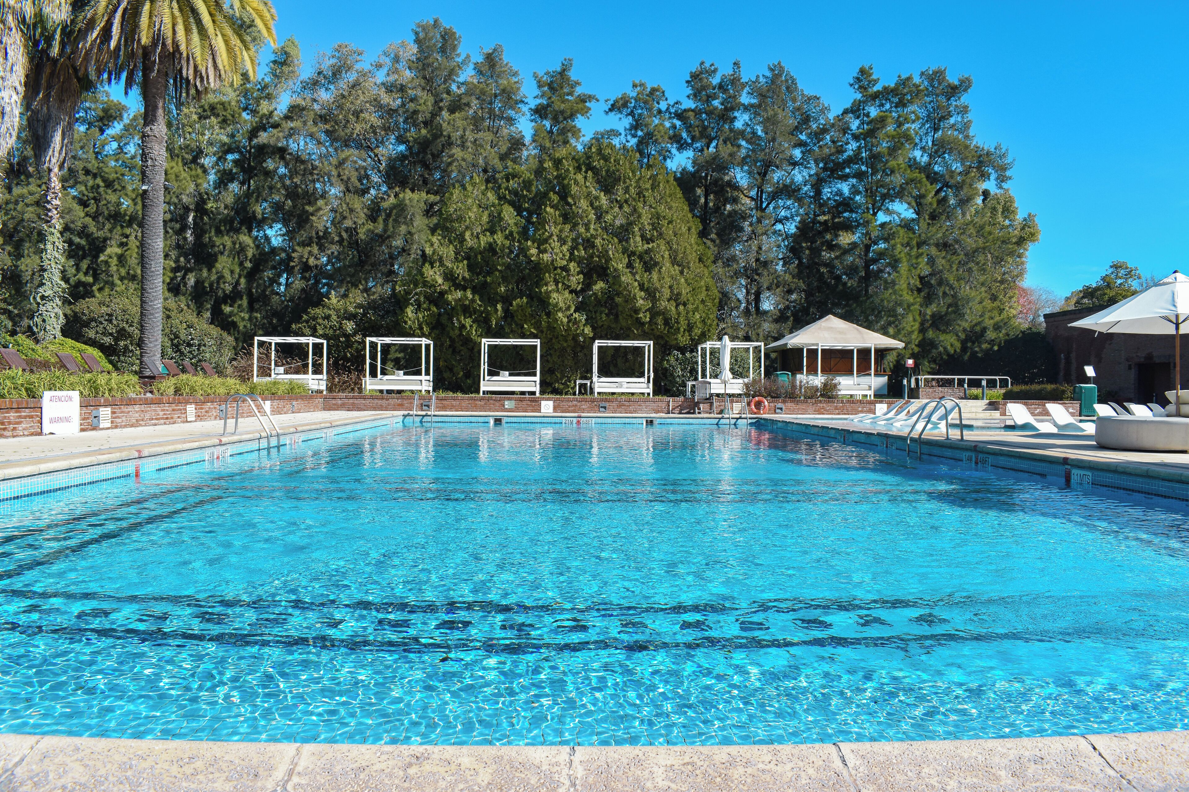 Una piscina con agua cristalina azul, rodeada de sillones de descanso y una zona de estar cubierta.