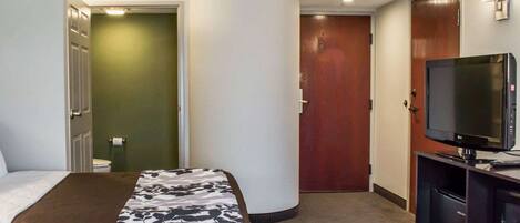A hotel room with a bed, a TV, a desk, and a door leading to another room.