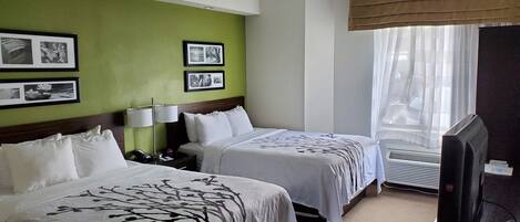 Habitación de hotel con dos camas, televisión y ventana con cortinas traslúcidas.