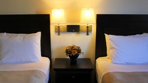 Habitación de hotel con dos camas, una mesita de noche con un florero y lámparas de pared.