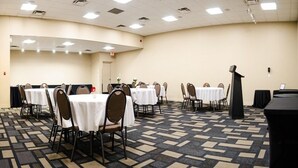 Un salón de conferencias con varias mesas y sillas, un atril y piso alfombrado.