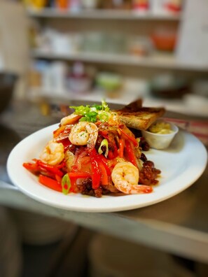 A plate of shrimp and vegetables with a side of bread and a small bowl of sauce. - Coronet Hotel Prince Albert (Prince Albert)