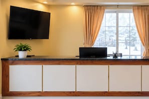 Un mostrador de recepción con un televisor de pantalla plana, una computadora portátil y una planta en maceta.
