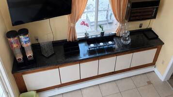 A kitchen with a black countertop, white cabinets, a TV mounted above, and a window with curtains.