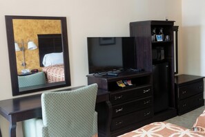 Une chambre d’hôtel comprenant un lit, un bureau avec une chaise, une télévision, un minibar et une armoire.