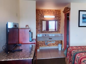 A room with a bed, a desk with a computer, a bathroom with a mirror and sink, and a framed picture on the wall. - Sunflower Inn Atlantic City Absecon (Galloway)