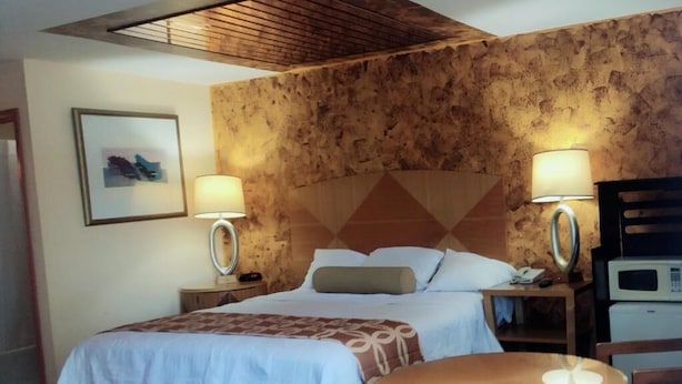 Una camera d'albergo con un letto, due lampade da comodino, un tavolo rotondo, una sedia e un forno a microonde.