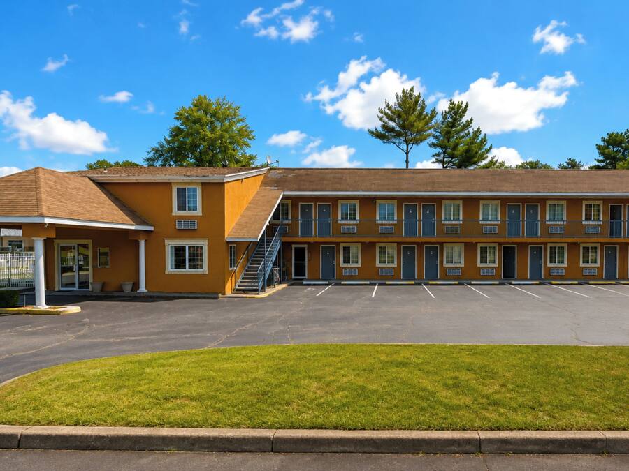 Um motel com estacionamento e área gramada na frente.